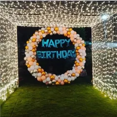 A magical birthday entrance created with a tunnel of fairy lights on a lawn. At the end of the tunnel, a circular balloon arrangement provides a perfect photo opportunity.