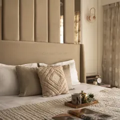 A close-up of the bed styling, showcasing the layered textures of the knitted bedspread and throw pillows. Details like the personalized mug and open magazine invite relaxation and add a personal touch.