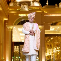 A grand portrait of the groom in his magnificent sherwani, standing before the beautifully lit wedding venue. A truly royal shot.
