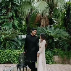 A stylish portrait set in a lush, tropical-themed courtyard. The blend of modern ethnic wear and green surroundings creates a look of contemporary elegance.