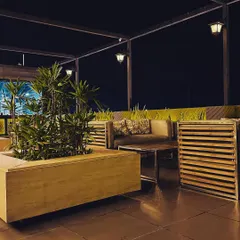 The seating area of a rooftop cafe we designed, featuring custom-built wooden furniture and large planters. The overhead pergola structure with hanging lanterns provides both architectural interest and ambient lighting for a comfortable dining experience.