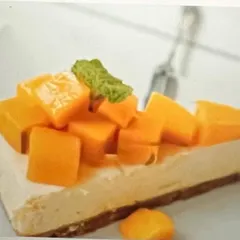 A professional shot of my plant-based mango cheesecake. You can see the creamy texture of the cashew-based filling and the generous topping of fresh mango chunks on a wholesome nutty crust.