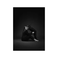In another tender moment from this series, the daughter leans in to whisper a secret to her mother. The dark studio setting enhances the intimacy and emotion of their connection.
