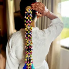 A getting-ready shot where the bride adjusts her hair, showing off the intricate details of the braid and her beautiful henna. It's a moment of quiet anticipation before the ceremony.