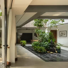 A view from a patterned tile patio into a home with a central green courtyard. The design creates a visual and physical connection between the outer garden and the inner sanctum, promoting a sense of continuous natural space.