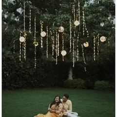 A magical evening portrait of the couple sitting on the grass under a tree adorned with beautiful hanging lights.