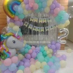 A dreamy unicorn-themed decoration for a 2nd birthday. We used a pastel rainbow balloon arch, a silver fringe curtain, and large unicorn and rainbow foil balloons to create a magical party space.