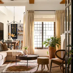 This angle of the living room shows the interplay of light and texture. The natural light from the large window highlights the different materials in the room, from the jute rug and rattan stool to the soft linen sofa and terracotta planter.
