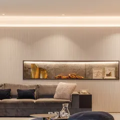 This living room corner exudes warmth and sophistication. We used a fluted wall panel to add subtle texture, enhanced by soft, indirect cove lighting. A recessed wall niche with its own backlighting creates a perfect display for decorative objects, showing how lighting can be used to craft mood and highlight details.