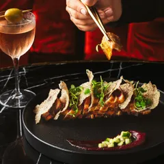 An interactive shot from the Akina Mumbai series, with chopsticks picking up a piece of sliced pork belly. This adds a human element and sense of action, complemented by a beautifully crafted cocktail.