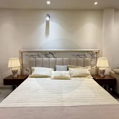 A perfect example of modern elegance. This custom bed features a headboard with a marble-patterned inlay and soft upholstered panels, flanked by classic table lamps for a serene and balanced look.