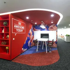 This creative huddle space at Scientific Games uses a bold red accent wall with the motivational phrase "Be Awesome Today." The high table and whiteboard are perfect for quick, standing brainstorming sessions.
