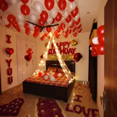 I create romantic birthday surprises at home, like this complete room decoration. It features a canopy with fairy lights over the bed, red and white balloons on the ceiling, and rose petals on the floor spelling out "I LOVE YOU".