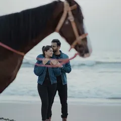 A close-up shot from the beach photoshoot with the horse, focusing on the couple's connection. The horse is framed in the foreground, adding depth and a storytelling element to this romantic portrait.