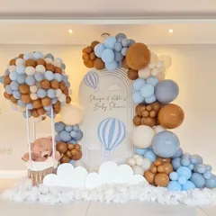 An elaborate 'Up, Up and Away' hot air balloon themed baby shower. This setup includes a large balloon sculpture forming a hot air balloon with a basket for a teddy bear, set against a custom backdrop and surrounded by clouds of balloons.