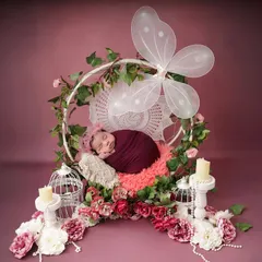 A magical, fairytale scene. This wide shot shows the newborn sleeping in a floral hoop with butterfly wings, surrounded by candles and birdcages for an enchanted forest feel.