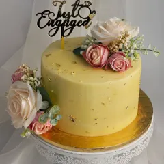 This "Just Engaged" cake is the definition of elegance. The smooth yellow buttercream is flecked with edible gold leaf and adorned with a mix of blush and cream artificial roses, all presented on a classic white lace stand.