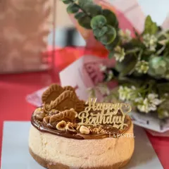 A full view of my eggless Nutella and Biscoff topped cheesecake, complete with a "Happy Birthday" topper and a flower bouquet.
