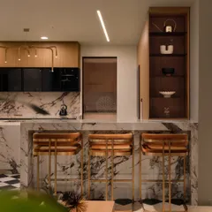A view from the living area into the kitchen, showing the marble bar counter with stylish wooden and brass stools. An open shelving unit provides space for display.