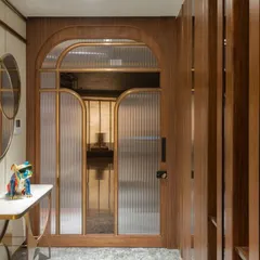 Here, the main door with its arched, fluted glass panels is designed to recede into a pocket, allowing the custom foyer console and vertical wood slat wall to take center stage. This creates a layered and welcoming entrance that feels both grand and intimate.