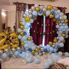 A home birthday decoration with a circular balloon arch in blue, silver, and gold, complete with large foil number balloons for the age.