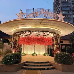 The main stage for a Navjote ceremony, featuring a "Navjote Mubarak" sign in lights. The stage is decorated with a canopy of red blossoms, creating a vibrant and celebratory focal point for the event.