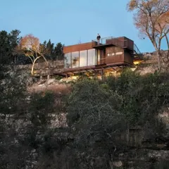 This is our vision for hillside living. A modular home built with a rustic, weathered steel exterior that blends into the rocky terrain, featuring a rooftop deck to take in the stunning views.