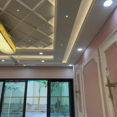 A close-up of an intricate false ceiling with a coffered design and a large, elegant light fixture. The pink walls with decorative molding add a touch of classic European style.