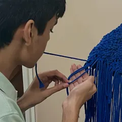 A close up of a student's hands as he practices a macrame knot. The focus required for this craft is incredibly relaxing.