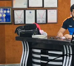 At my desk in the academy, with my own medals and certificates in the background. I lead by example, and my personal achievements are a testament to the path of success I guide my students on.