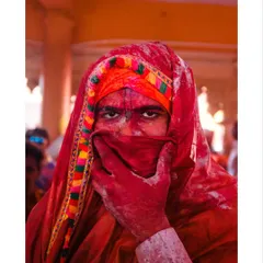A portrait from the Holi festival, where a man's intense gaze pierces through a veil of vibrant red powder. This image captures the raw, visceral energy of the celebration.