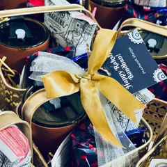 A close-up of our Rakhi hamper, showcasing the rich textures of the golden metal basket, the leather-clad tumbler, and the satin ribbon, all tied together with a personalized tag.