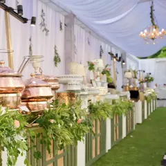 An expansive view of an elegant buffet setup for an outdoor corporate luncheon. Our signature hammered copper serveware and fresh floral arrangements create a visually stunning centerpiece for any gathering.