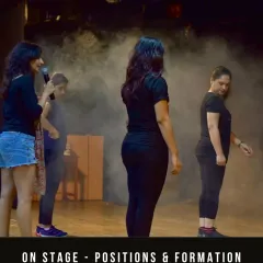 An instructor works with students on stage positioning and formation. Learning how to use the stage space effectively is a key part of transforming a dancer into a performer.