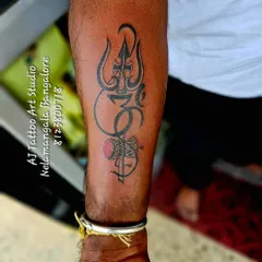 A powerful forearm tattoo combining the Trishul, Om symbol, and a Damaru with a splash of red. This is a classic and popular spiritual design.