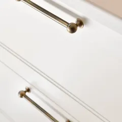 Our Sphere cabinet pulls in an antique brass finish, installed on the drawers of a kitchen island. The simple, clean design provides a touch of vintage elegance to the soft white cabinetry.