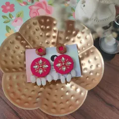 A close-up of my hand-painted fabric earrings. This pair features intricate white and gold floral patterns on a bright pink base, with delicate white bead drops for a festive look.