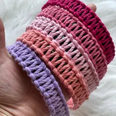 Holding a selection of my handmade macrame hairbands to show their texture and vibrant colors. This stack includes shades of lavender, peach, and multiple tones of pink, highlighting the detailed knotwork.