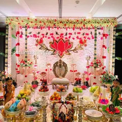 A wide-angle shot of the puberty ceremony decoration. The symmetrical arrangement of offering plates, dolls, and floral elements creates a balanced and visually stunning scene.