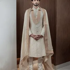 For the groom who desires nothing less than royalty. This ivory sherwani, complete with a regal cape and a multi-layered pearl necklace, is designed to make a grand statement on your most important day.
