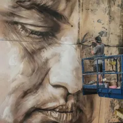 Australian artist Guido Van Helten at work on a massive portrait at Sassoon Dock. This shot, showing him high up on a lift, gives a sense of the scale and effort required for these monumental murals.
