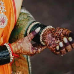 A beautiful shot of the bride's hands, showcasing the rich, dark mehendi stain against her traditional wedding attire and bangles.
