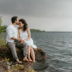 A tender moment between a couple sitting by the water's edge, with moody skies overhead. This captures a quiet, intimate connection.