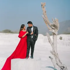 A classic pose with a dramatic twist. The couple stands together in a surreal white location, her long red dress trailing behind, creating a powerful and artistic pre-wedding photograph.