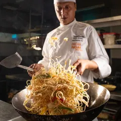 Capturing the chef's skill with a dynamic shot of noodles being tossed high in a wok. The motion blur conveys energy and heat.
