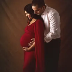 A classic and intimate portrait in a bold red gown. The dark, moody lighting and the husband's gentle embrace from behind create a powerful and romantic image focused on the couple's connection.