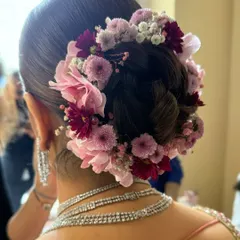 This bridal bun is adorned with a beautiful arrangement of pink and burgundy chrysanthemums and baby's breath, creating a full and vibrant floral crown.