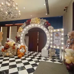 We love creating impressive entryways. This setup for a first birthday features a large marquee-light arch, a warm-toned balloon garland, and cute teddy bear props, all leading to a custom-lit photo stand for the event.