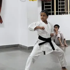 A young black belt student demonstrates a sharp technique during her belt exam, holding a strong stance that shows focus and control.