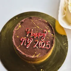 A mini chocolate cake with "Happy NY 2025" piped on top, perfect for a small celebration.